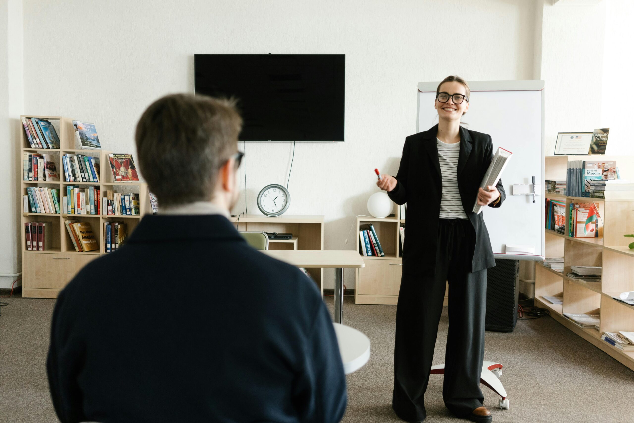 Bizneswoman prowadząca prezentację w biurze z półkami na książki i zegarem.